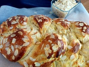 Braided Sweet Bread sprinkled with almond slices on a baking parchment.