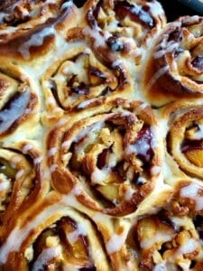 Close-up of baked Plum Cinnamon Rolls drizzled with glaze. 