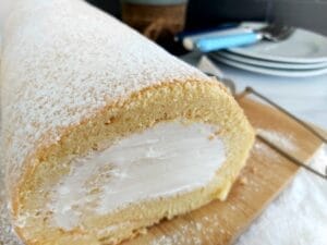 With icing sugar dusted Lemon Swiss Roll on a wooden platter.