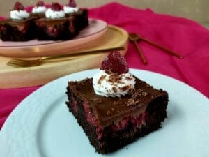 Chocolate Cake slice topped with raspberry on a white plate