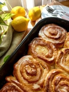 Golden baked lemon curd rolls in a baking dish with fresh lemons in the background. 