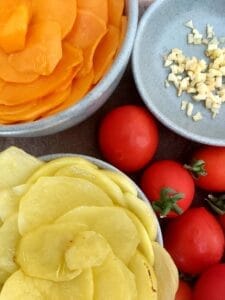 Image showing sliced potatoes, sliced sweet potatoes, cocktail tomatoes, and minced garlic.