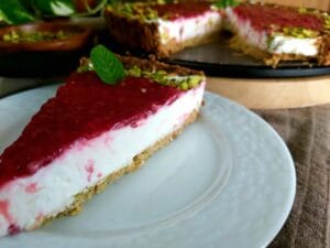 Slice of a Pistachio Raspberry Tart on a white plate with the Tart in the background.