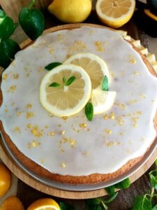 A round cake glazed with lemon glaze and topped with slices of lemon, lemon zest, and mint leaves.