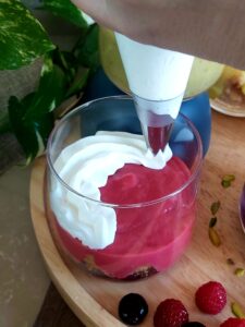 Piping whipped cream onto colourful fruit curd in a glass.