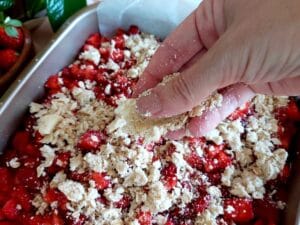 Spreading the crumble topping evenly over the strawberry layer.