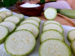 Sliced zucchini on a white tablecloth, sprinkled with salt to release excess liquid.