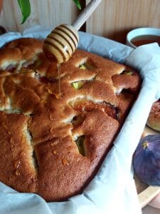 Close-up of golden honey being drizzled over a baked fig and walnut cake.