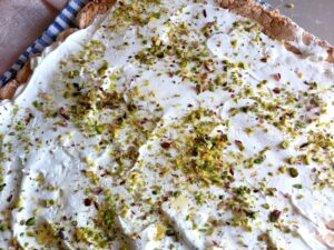 A baked pavlova sheet unrolled on a kitchen towel with filling spread evenly over the surface.