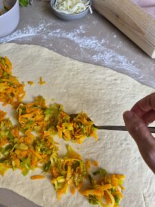 Sautéed vegetable being spread out onto a rolled out dough. 