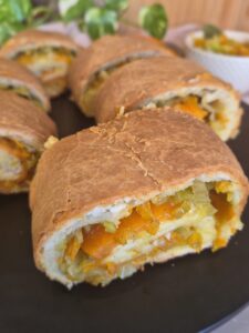 Golden baked slices of a winter vegetable roll on a black platter.
