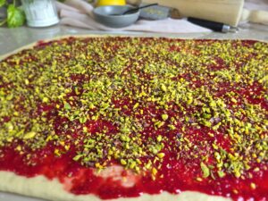 Close-up of rolled out dough, spread with thin layer of raspberry filling & chopped pistachios.