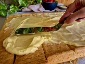 Spreading vanilla pastry cream over even strips of the sponge base.