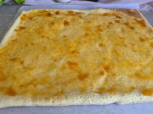 Thin layer of apricot jam spread on a golden baked sponge base.