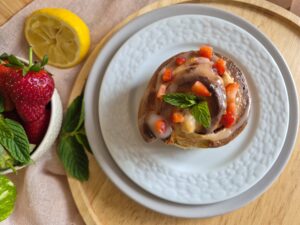 Strawberry-Mint Cheesecake Rolls on a white plate garnished with fresh strawberries and mint leaves. 