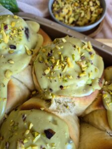 Close-up of golden baked Pistachio Lemon Rolls topped with pistachio cream and sliced pistachios.