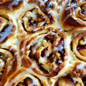 Close-up of baked Plum Cinnamon Rolls drizzled with glaze.