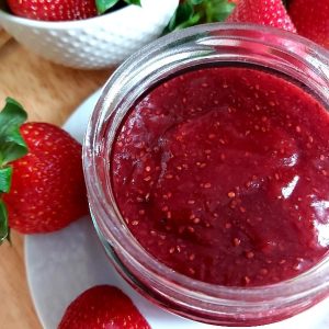 Jar filled with strawberry jam on a white plate garnished with fresh strawberries