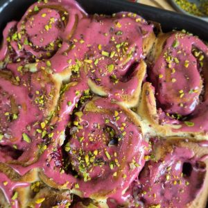 Close-up of golden baked Raspberry Rose Rolls topped with raspberry glaze and sprinkled with chopped pistachios.