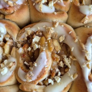 Close-up of golden baken Apple Cinnamon Rolls topped with glaze and chopped walnuts.