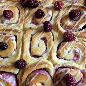 Close-up of golden baked soft lemon blackberry sweet rolls, drizzled with lemon glaze and topped with fresh blackberries.